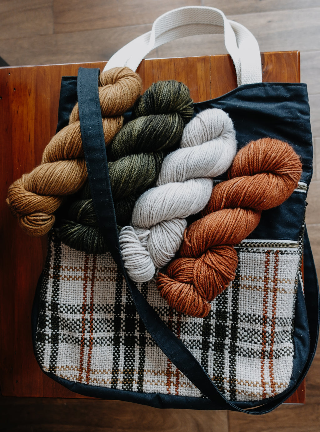A black canvas and white and orange flannel project bag lays on a chair. Four skeins of yarn sit on top, showing they would fit comfortably inside.