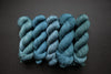 Five skeins of yarn, all different bases, are naturally dyed an indigo blue. They are lined up in a row on a black surface.