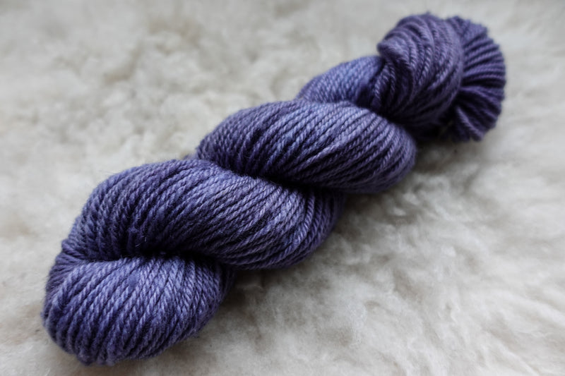A skein of purple hand dyed yarn lays on a wool background.