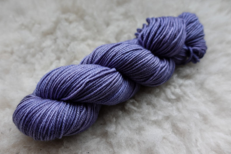 A worsted weight skein of yarn has been naturally dyed purple. It lays on a wool background.