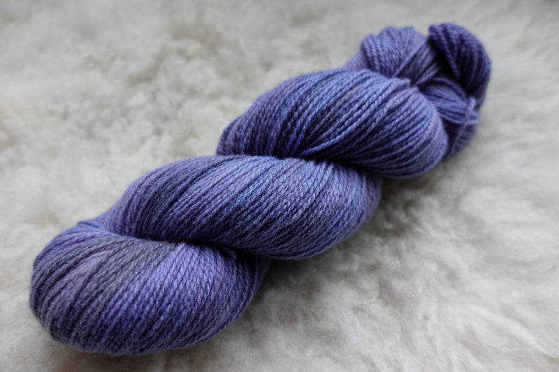 A skein of purple, hand dyed yarn lays on wool.