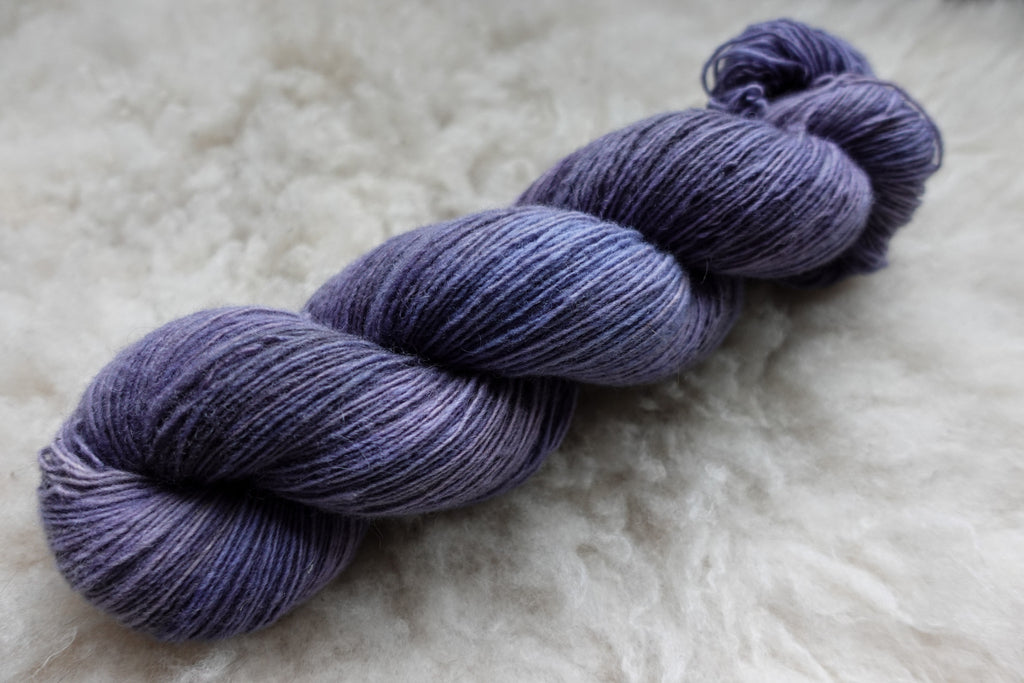 A skein of single ply yarn lays on wool. It has been hand dyed purple.