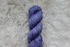 Pictured up close, a hand dyed skein of purple yarn lays on wool.