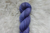 A skein of naturally dyed purple yarn lays on a wool background.