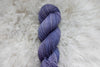 A skein of purple, natural fiber yarn lays on wool.