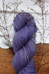 A skein of naturally dyed purple yarn lays on a tabletop. Sprigs of budding twigs are laid next to it.