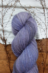 A naturally dyed skein of purple, fingering weight yarn lays on a tabletop. 