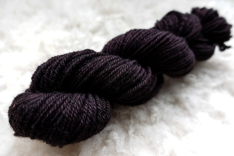 A skein of worsted weight yarn lays on wool. It has been naturally dyed a dark burgundy.