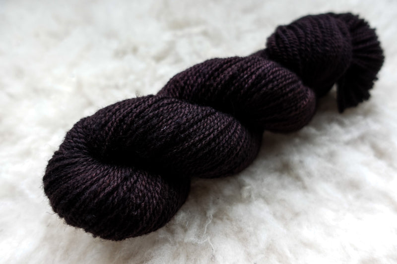 A skein of dark burgundy, hand dyed yarn lays on wool.