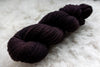 A skein of sport weight yarn has been hand dyed a dark burgundy. It lays on a wool background.