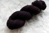 A skein of fingering weight, single ply yarn has been naturally dyed a dark burgundy.