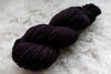 A skein of fingering weight, natural fiber yarn has been hand dyed a dark burgundy. 