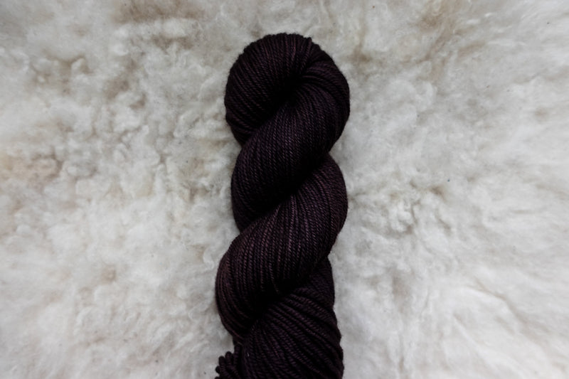 A dark burgundy skein of natural fiber yarn lays on wool.