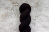 A skein of natural fiber yarn lays on a wool background. It has been dyed a dark burgundy.