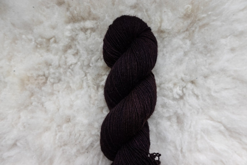 A skein of natural fiber yarn has been hand dyed a dark burgundy. It lays on a wool background.