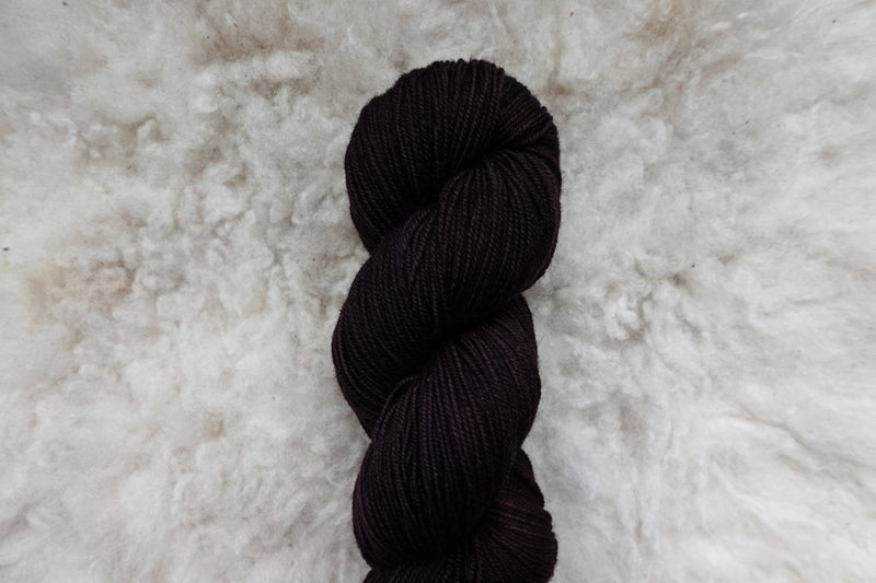 A dark burgundy skein of naturally dyed yarn lays on wool.