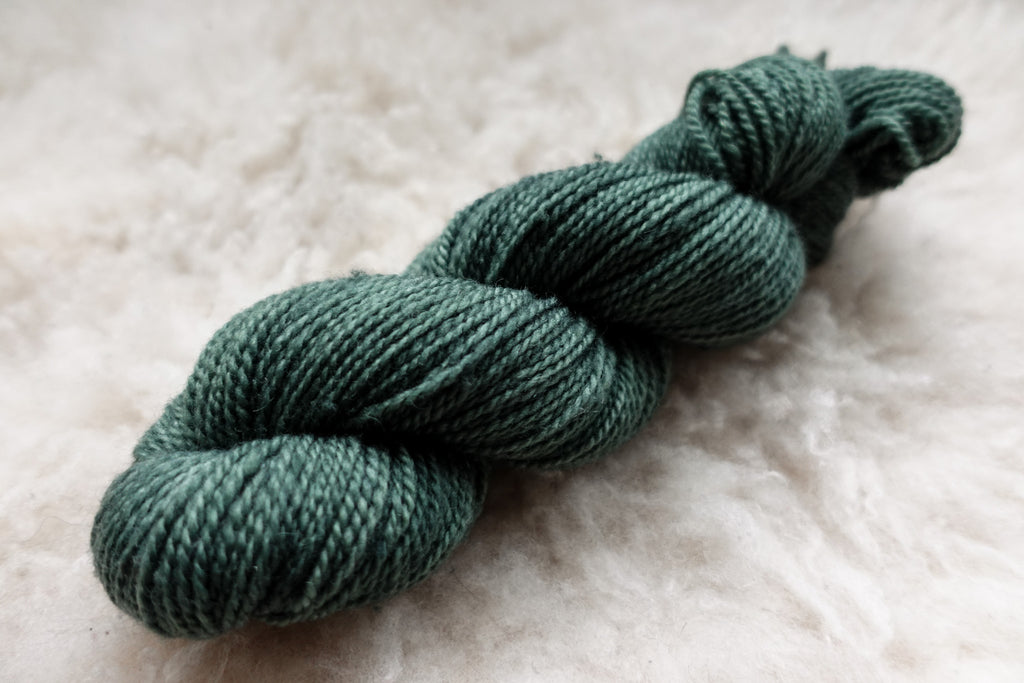 A blue green skein of hand dyed yarn lays on a wool background.