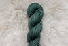 A blue green skein of naturally dyed yarn lays on a wool tabletop.