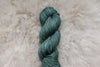 A naturally dyed skein of blue green yarn lays on a wool background.