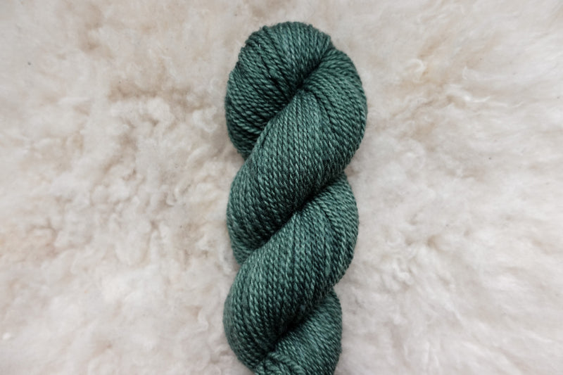 A hand dyed skein of blue green yarn lays on a wool background.