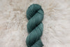 A blue green skein of natural fiber yarn lays on a wool background.