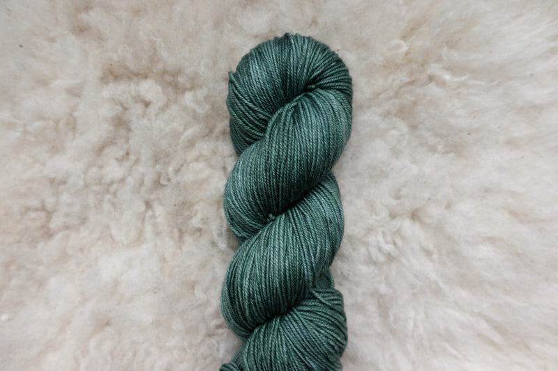 A skein of natural fiber yarn has been dyed blue green, and lays on a wool background.