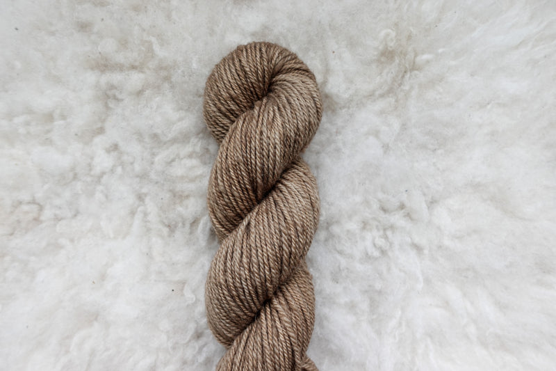 Pictured from above, a light beige skein of naturally dyed yarn lays on a sheepskin rug.