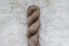 Pictured from above, a light brown skein of naturally dyed yarn lays on a sheepskin rug.