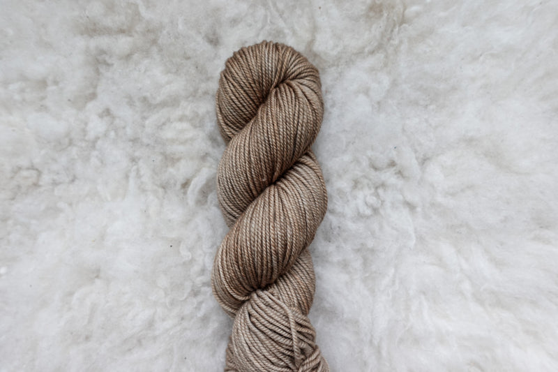 Pictured from above, a light brown skein of naturally dyed yarn lays on a sheepskin rug.