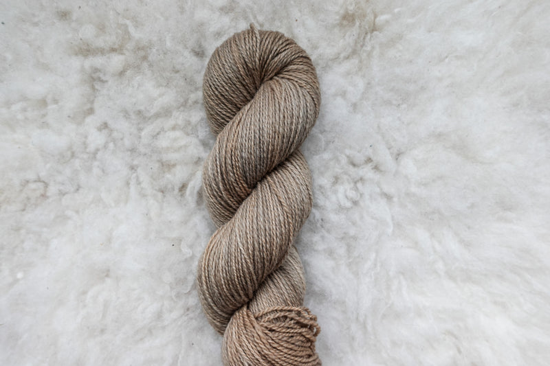 Pictured from above, a light beige skein of naturally dyed yarn lays on a sheepskin rug.