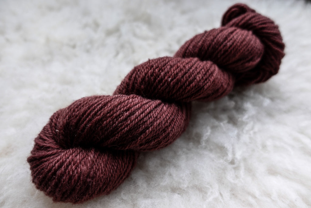 A reddish pink skein of naturally dyed yarn lays on a sheepskin rug.