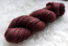 A skein of natural fiber yarn has been hand dyed reddish pink. It lays on a sheepskin rug.