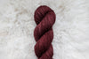 A reddish pink skein of naturally dyed yarn lays on a sheepskin rug, pictured from above.