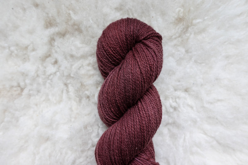 A reddish pink skein of natually dyed yarn lays on a sheepskin rug, pictured from above.