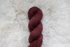 A naturally dyed skein of reddish pink yarn lays on a sheepskin rug, pictured from above.