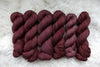 Six skeins of yarn, all different bases, have been hand dyed a reddish pink. They lay on a sheepskin rug.