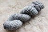 A light grey skein of naturally dyed yarn lays on a sheepskin rug.