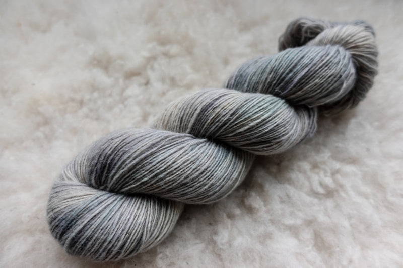 A skein of light grey, natural fiber yarn lays on a sheepskin rug.