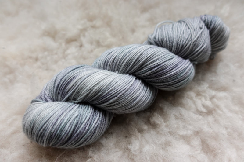 A light grey skein of natural fiber yarn lays on a sheepskin rug.
