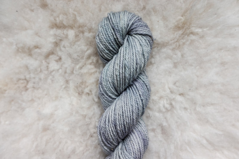 Pictured from above, a light grey skein of naturally dyed yarn lays on a sheepskin.