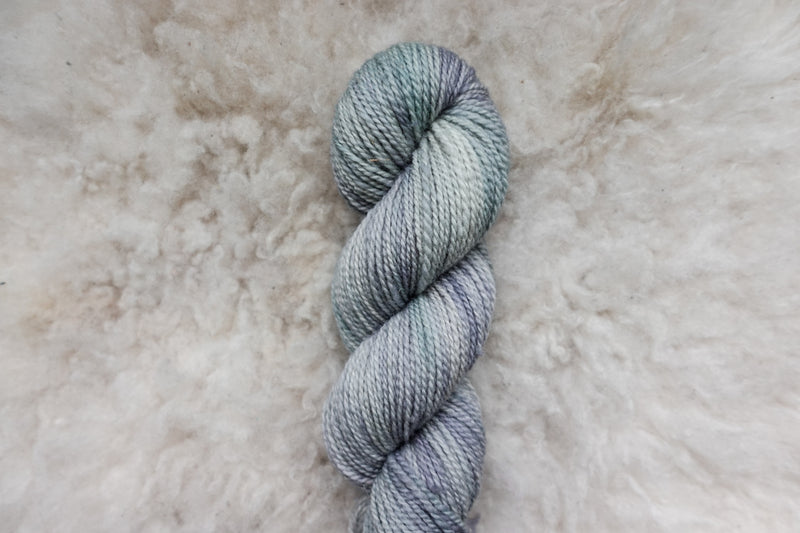 A light grey skein of naturally dyed yarn lays on a sheepskin rug, pictured from above.