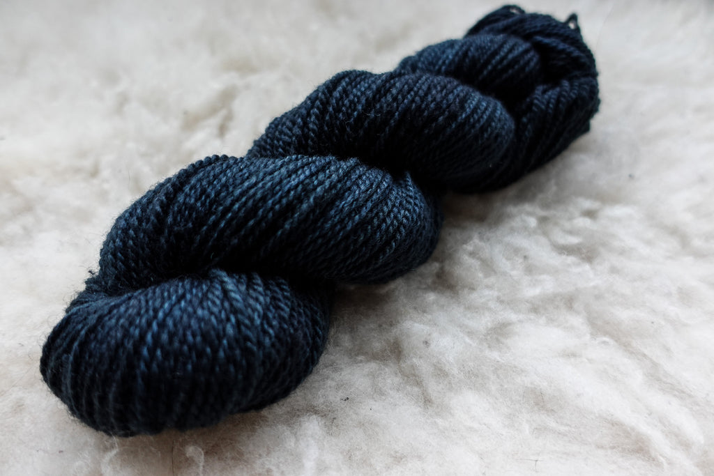 A deep blue, naturally dyed skein of yarn lays on a sheepskin rug.