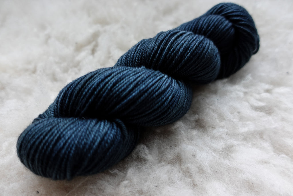 A natural fiber skein of deep blue yarn lays on a sheepskin rug.