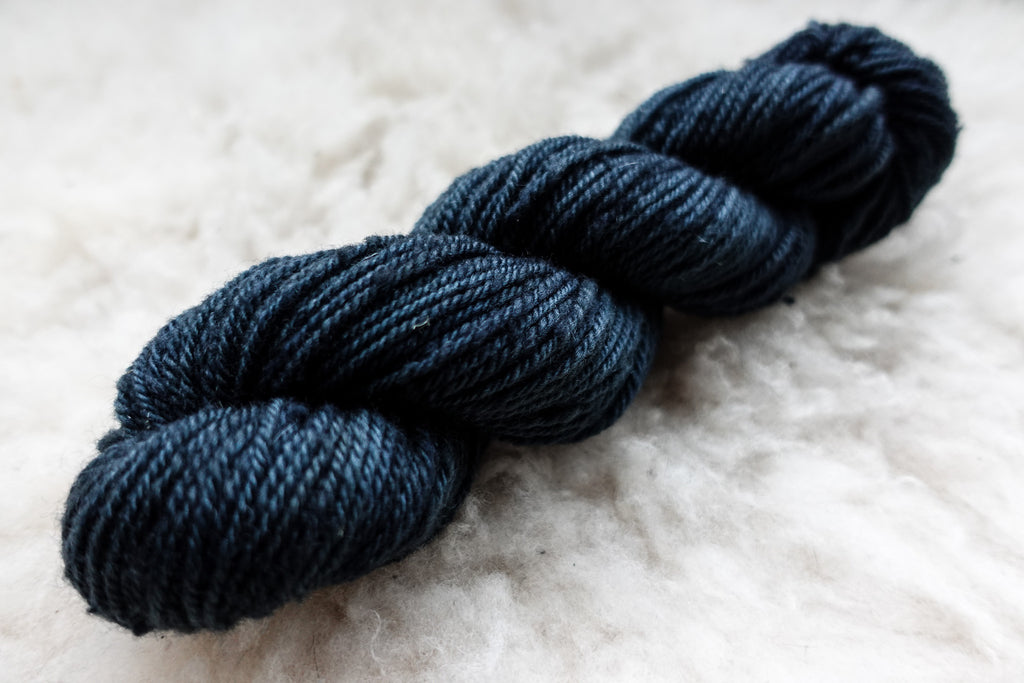 A natural fiber skein of yarn has been dyed a deep blue. It lays on a sheepskin rug.