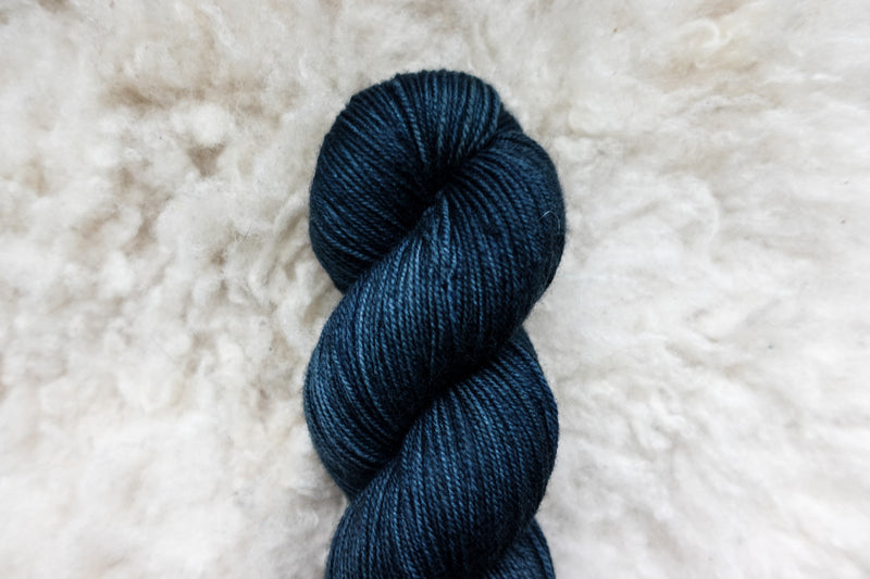 Pictured from above, a deep blue skein of natural fiber yarn lays on a sheepskin rug.