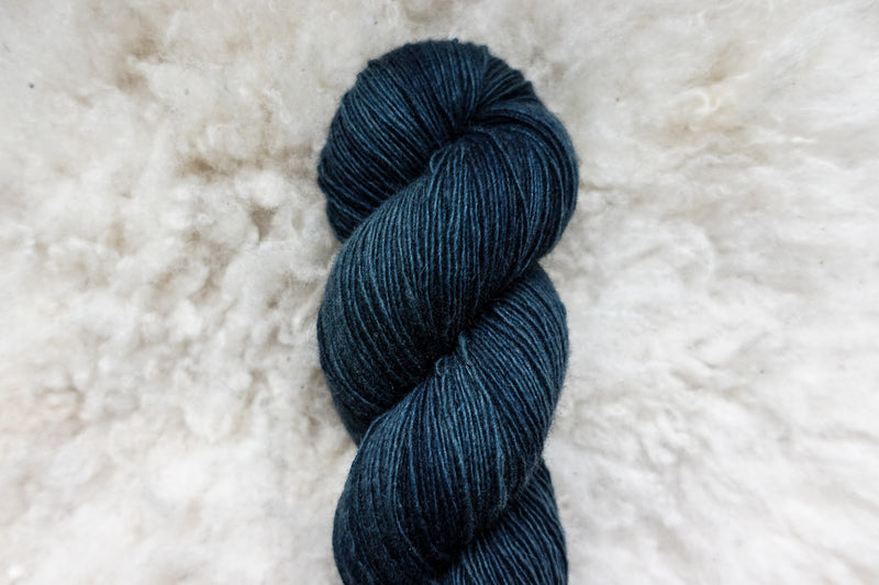 Pictured up close, a skein of naturally dyed, deep blue yarn lays on a sheepskin rug.
