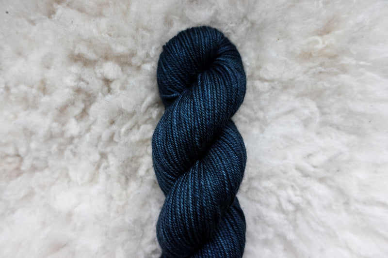 Pictured from above, a hand dyed skein of deep blue yarn lays on sheepskin.