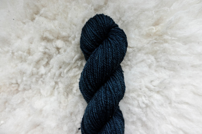 Pictured from above, a hand dyed skein of deep blue yarn lays on a sheepskin rug.
