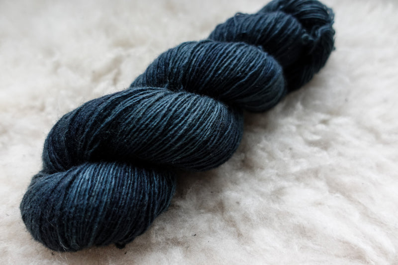 A skein of natural fiber yarn, hand dyed deep blue, lays on a sheepskin rug.