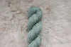 A skein of yarn, naturally dyed a light grey, lays on a sheepskin and is pictured from above.